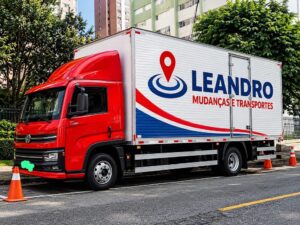 Caminhão baú vermelho da Leandro Mudanças e Transportes em frente a edifícios residenciais, ilustrando a vistoria de escadas e elevadores antes da mudança.