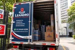 Caminhão baú vermelho da Leandro Mudanças e Transportes em frente a edifícios residenciais, ilustrando como registrar acessos do prédio antes da mudança.